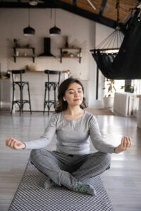 A woman meditates peacefully on a yoga mat indoors, promoting mindfulness and relaxation.