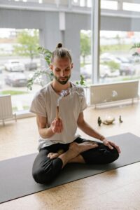 Man meditating in a bright room, holding Palo Santo while sitting in lotus position.
