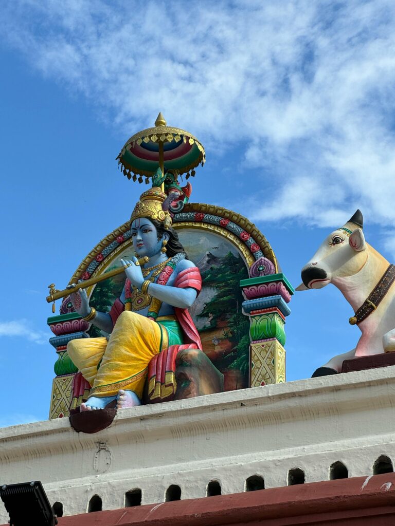 Vibrant Hindu sculpture atop temple, showcasing deity and sacred cow under clear sky.
