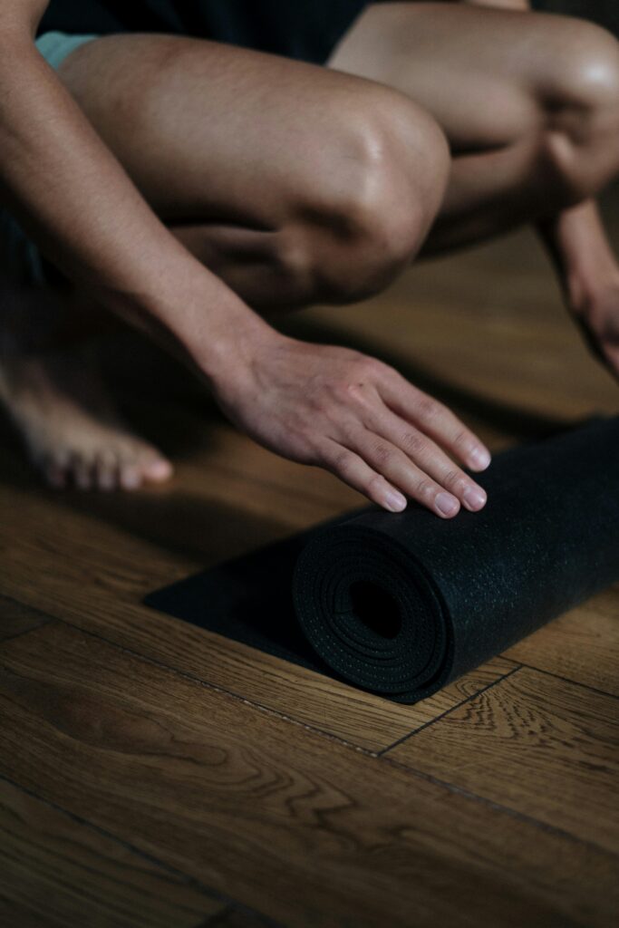 Close-up of a man rolling up a yoga mat on a wooden floor in a yoga studio.