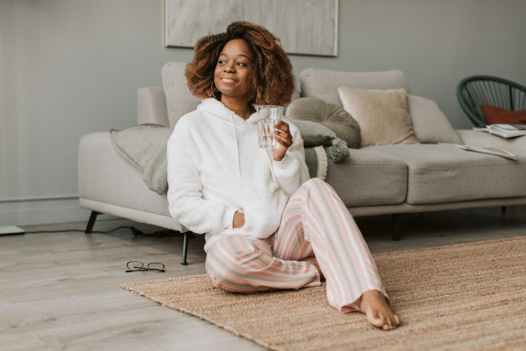 An African American woman enjoys a relaxing morning indoors, sitting with a glass of water.