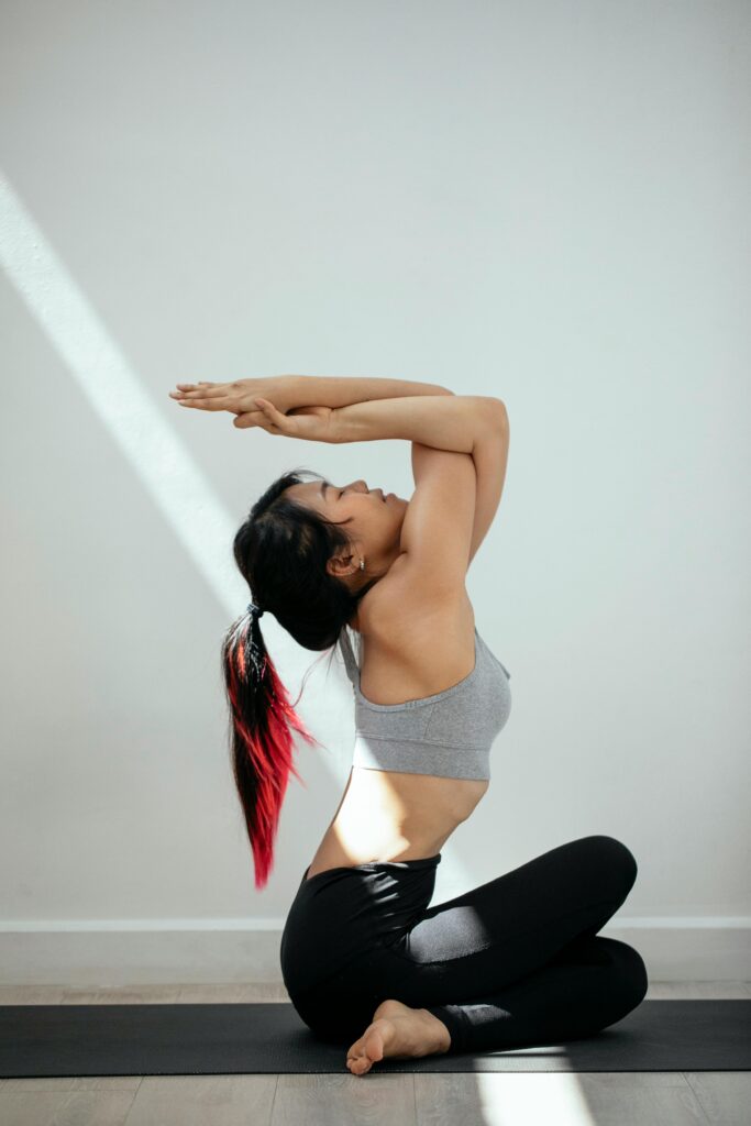 Side view of slim Asian female with closed eyes and in sportswear performing Cow Face pose during yoga session on floor against white wall