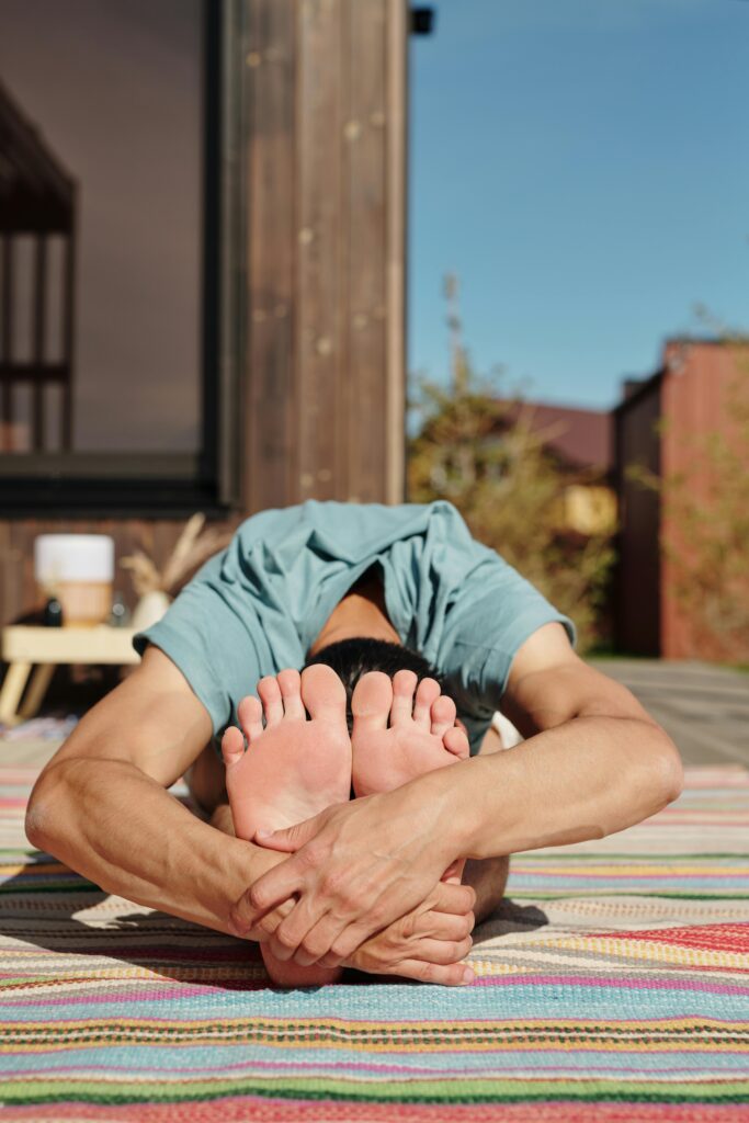 Man performing a seated forward fold yoga pose on a vibrant mat outdoors for relaxation.